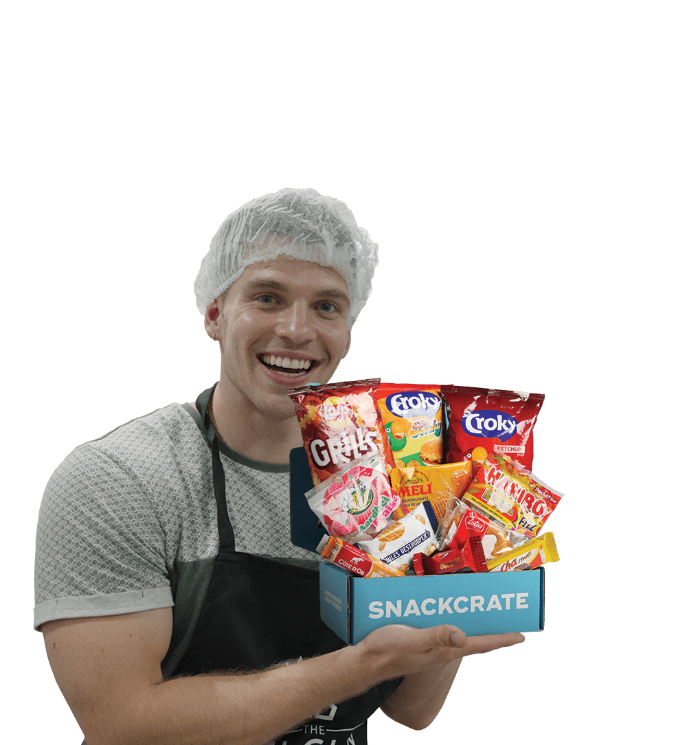 Bryson wearing a hair net and apron holding an open Belgian SnackCrate overflowing with snacks.